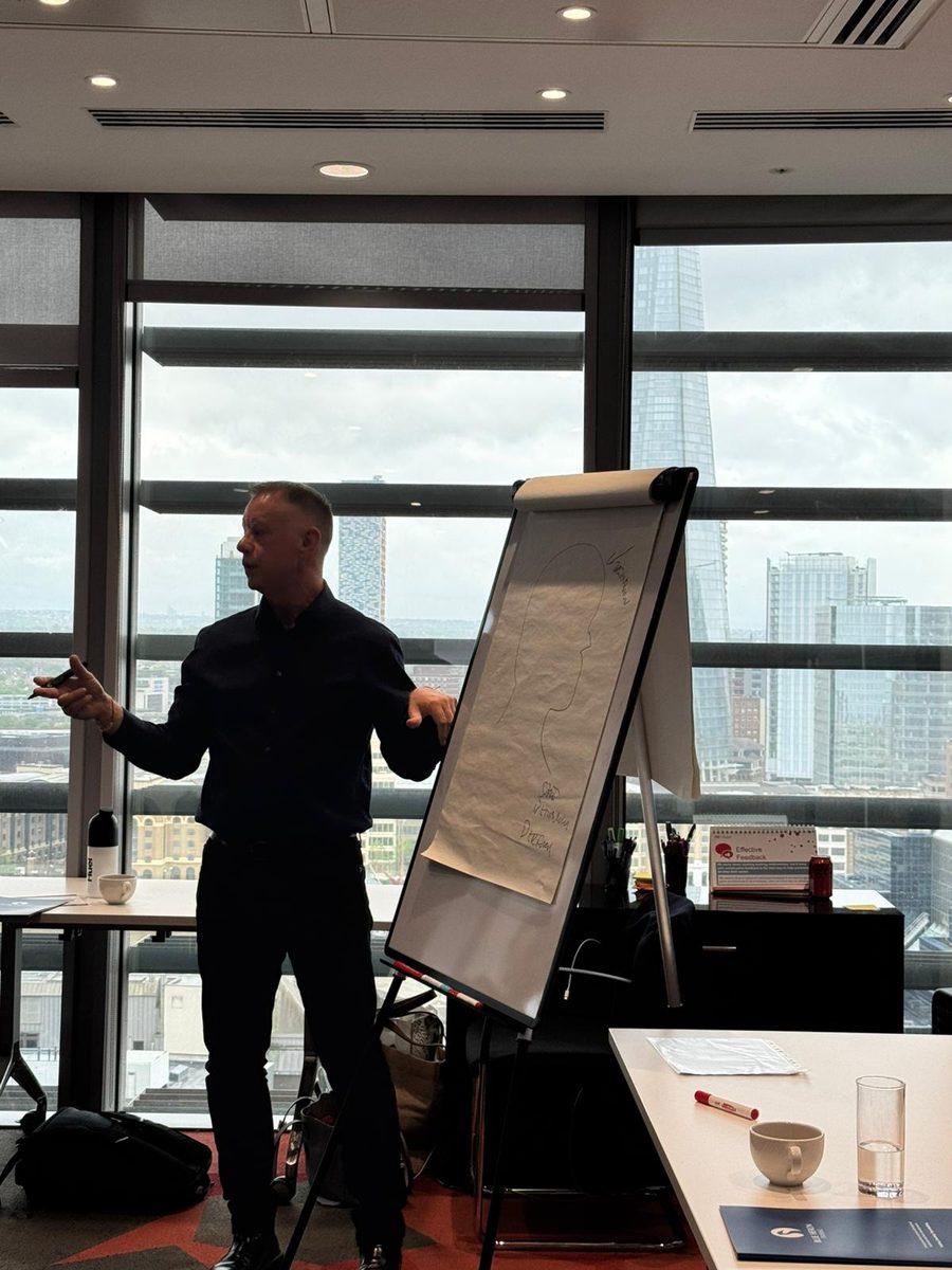 Paul Ward at a flipchart in a high-rise meeting room, explaining a drawing of a head